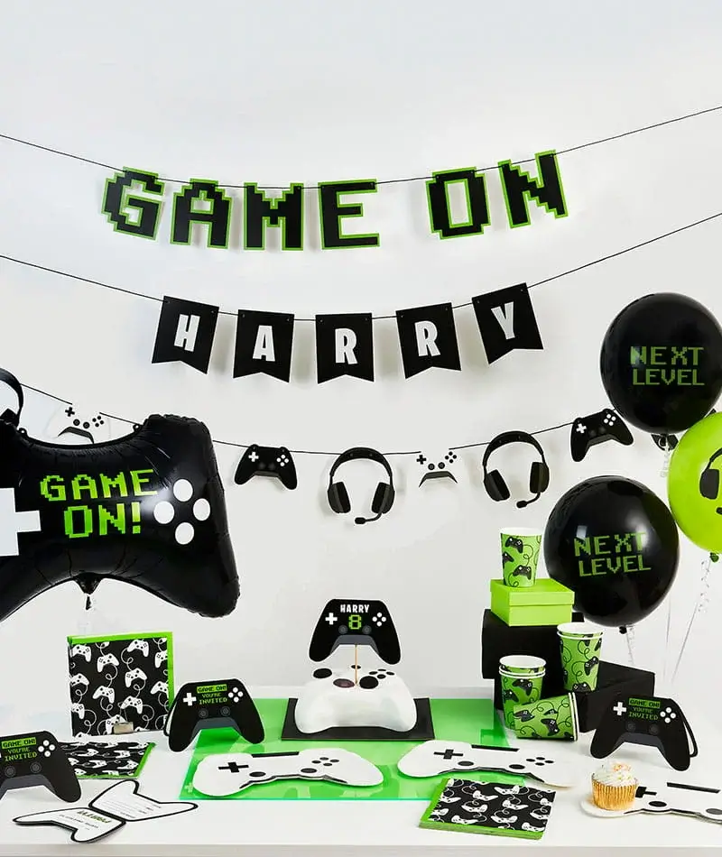 Gaming-themed birthday party display with console controller decorations, balloons, party tableware, a birthday Gaming-themed birthday party display with console controller decorations, balloons, party tableware, a birthday